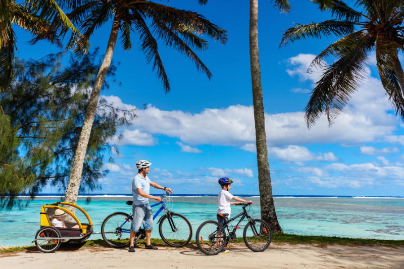 Father and kids enjoy a bike ride alongside the beautiful beaches of Rarotonga